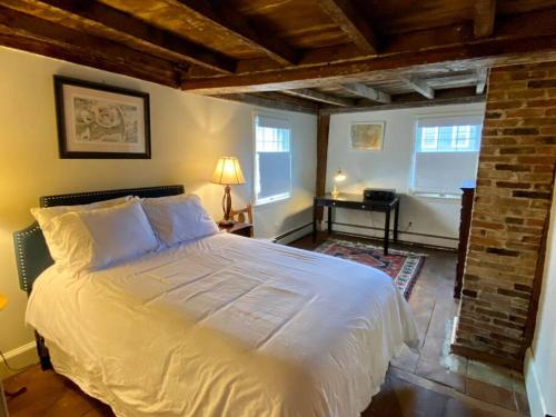 1 dormitorio con cama blanca y pared de ladrillo en Circa 1725 home w/Roof Deck and Water Views en Newburyport