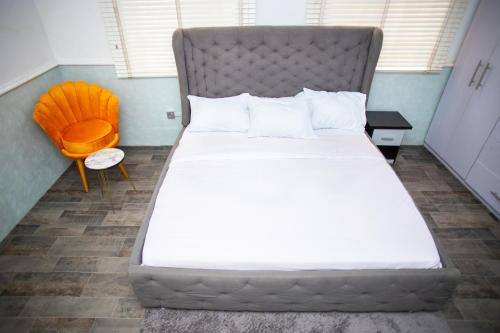 a large bed in a room with a orange chair at House 55 Apartments in Abuja