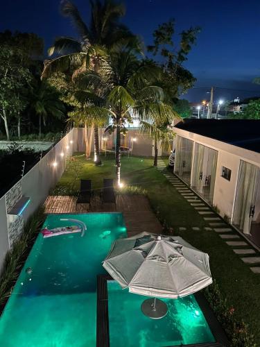 a swimming pool with an umbrella next to a house at Cantinho do sossego in Porto Seguro