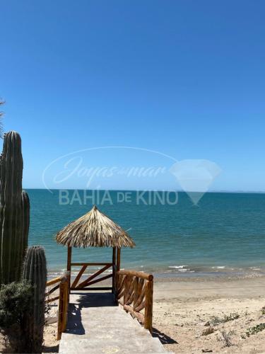 a beach with a straw umbrella and the ocean at Esmeralda Joyas Del Mar Bahia de Kino in Bahía Kino