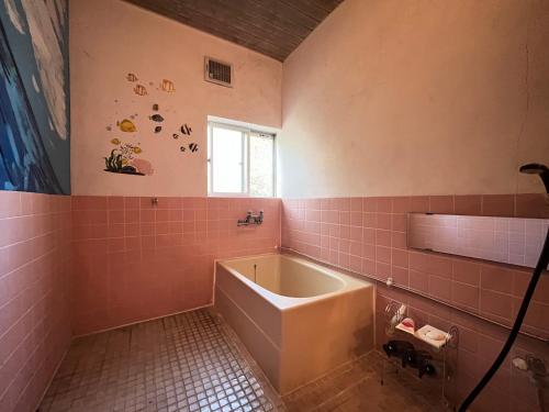 a bathroom with a tub and pink tiled walls at 民宿かず in Sosa