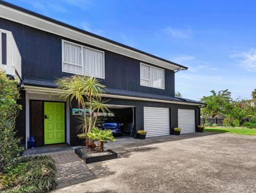 a black and white house with a green garage at Coastal Oasis - Papamoa Beach Holiday Home in Papamoa
