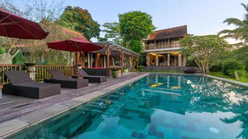 una piscina con sillas y sombrillas junto a una casa en Ayawana Private Villas Managed by ARM Hospitality, en Tegalalang