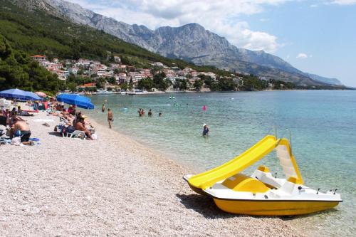 a yellow boat on a beach with people in the water at Apartments with a parking space Brela, Makarska - 17371 in Brela