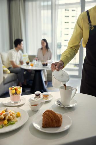 una persona che versa caffè in una tazza su un tavolo con cibo di Dusit Suites Hotel Ratchadamri, Bangkok a Bangkok