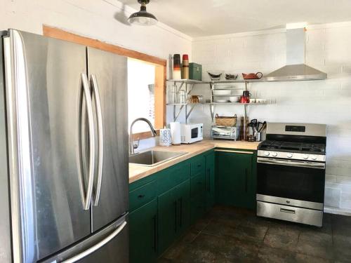 a kitchen with green cabinets and a stainless steel refrigerator at JT's Star Catcher Cabin - HOT TUB in Yucca Valley