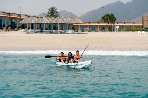 three people in a boat on the water near a beach at Royal Beach Hotel & Resort in Dibba