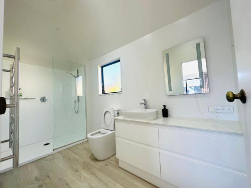 a white bathroom with a toilet and a sink at Spacious Mission Bay Villa 100m to the beach, seaview, private garden, Netflix in Auckland