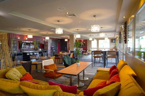 a restaurant with yellow couches and tables and chairs at Best Western l'Atelier 117 in Maubeuge