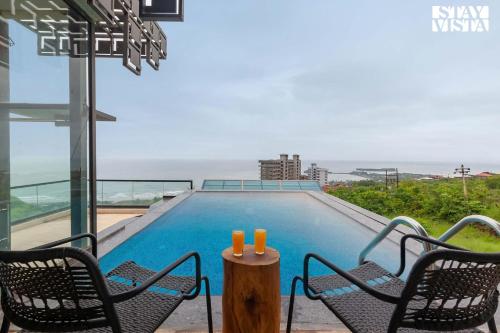 een zwembad met twee stoelen en een tafel met twee kaarsen bij StayVista Sea Pearl View Beach View with Rooftop Pool in Dapoli