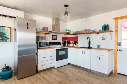 a kitchen with white cabinets and a stainless steel refrigerator at KAMPINK! Pool, Spa, Gameroom Compound with Amazing Views on 2.5 Acres in Joshua Tree