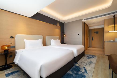 two beds in a hotel room with white sheets at Langham Honor International Hotel Canton Fair Complex Kecun Metro Station Branch - Free Shuttle Bus to Canton Fair Complex During Canton Fair Period & Free Deliver Service to Guangzhou Baiyun International Airport in Guangzhou
