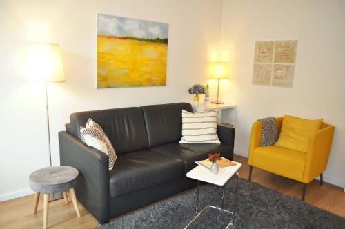 ein Wohnzimmer mit einem schwarzen Sofa und einem gelben Stuhl in der Unterkunft App 44 Seestern Ferienwohnung in Timmendorfer Strand