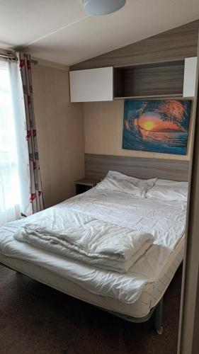 a bedroom with a white bed with a painting on the wall at 3 BEDROOM CARAVAN ON ST OSYTH BEACH HOLIDAY PARK WITH FREE Wfi AND PARKING in Saint Osyth