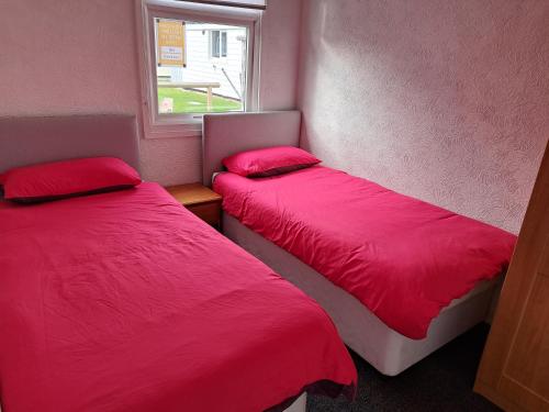 two beds in a room with red sheets and a window at Cosy 2-Bed Chalet in Bridlington - Free WiFi in Bridlington