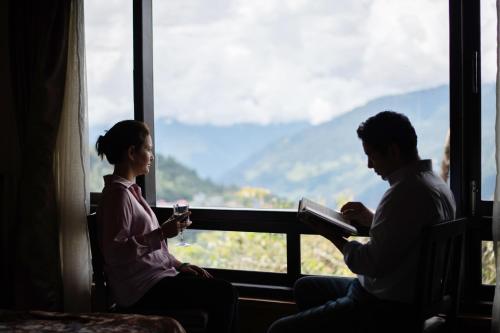 mężczyzna i kobieta siedzący w oknie z książką i szklanką w obiekcie StayVista's Himalayan Horizon - Mountain & Valley-View Villa with Heater w mieście Gangtok