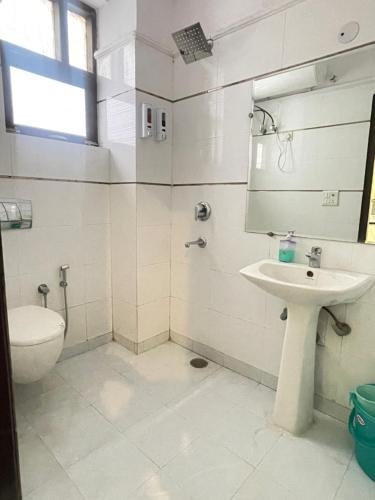 a white bathroom with a toilet and a sink at Aadi's Residency in Gurgaon