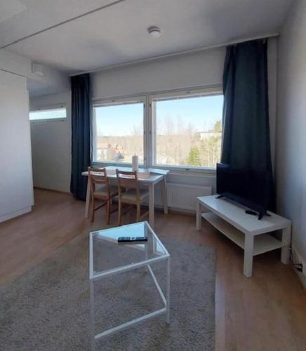 a living room with a table and a tv and a window at Kotimaailma - Valoisa kalustettu yksiö Espoossa in Espoo