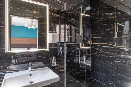 a black bathroom with a sink and a mirror at The Originals Boutique, Hôtel Le Marignan,Le Havre Centre Gare in Le Havre