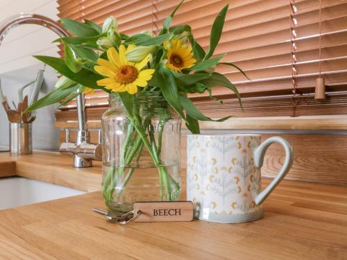 a vase filled with yellow flowers sitting next to a mug at Beech in Kemble