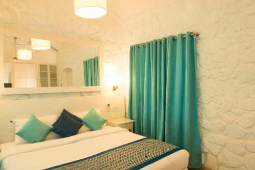 a bedroom with a bed with a mirror and green curtains at The Tamarind Hotel - A Boutique Heritage Stay, Anjuna - Goa in Anjuna