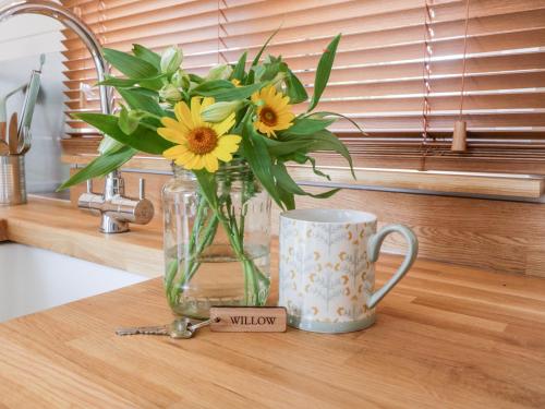 a vase of flowers sitting on a counter next to a mug at Willow in Kemble
