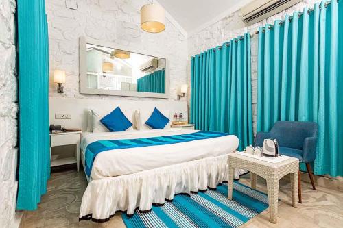 a bedroom with a bed with blue curtains and a mirror at The Tamarind Hotel Goa in Anjuna