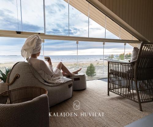 a woman sitting on a couch looking out at the beach at Marina Resort B11 in Kalajoki