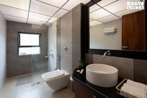 a bathroom with a sink and a toilet and a mirror at Otonia by StayVista with Indoor swimming pool, Modern interiors & a mix of indoor & outdoor games in Panchgani