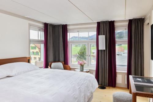 a bedroom with a white bed and a large window at Appenzeller Huus Löwen in Gonten