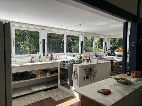 a large kitchen with white counters and windows at Schönes Haus direkt am Fluß in der Mata Atlantica in São Sebastião