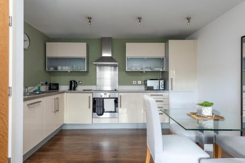 a kitchen with white cabinets and a glass table at City Stay Apartments - Vizion in Milton Keynes