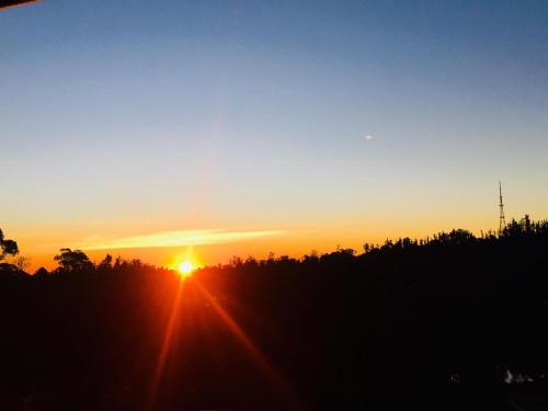 a sunset with the sun setting over a forest at Maruti Villa in Kodaikānāl