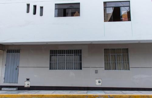 a white building with four windows and a door at Confortable habitación doble frente al Aeropuerto in Lima
