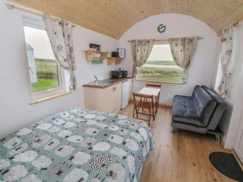 a bedroom with a bed and a chair and two windows at The Snuggly Sheep Farm Stay Shepherd Hut in Ballyshannon