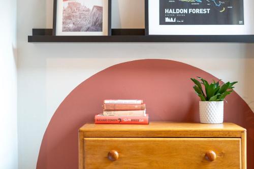 a stack of books on a wooden dresser with a plant on it at Chic Townhouse in the heart of Historical Exeter 5mins to Centre in Exeter