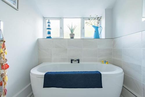 a bathroom with a white tub and a window at Driftwood - Charming family home in Deal