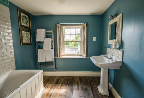 ein blaues Badezimmer mit einem Waschbecken, einer Badewanne und einem Fenster in der Unterkunft George and Dragon Clifton in Penrith