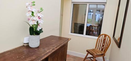 a vase of flowers on a wooden table with a chair at Beautiful Spacious 5 Bed House in Fornham Saint Martin