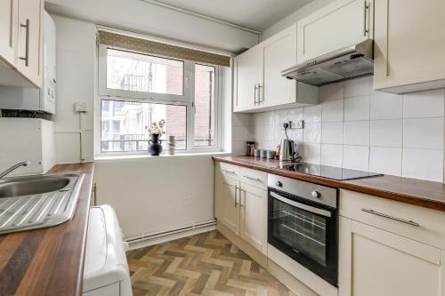 uma cozinha com armários brancos, um lavatório e uma janela em Central NW1 London Apartment! em Londres