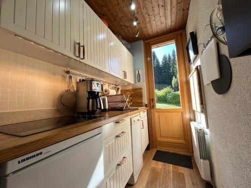 Elle comprend une petite cuisine avec des placards blancs et une fenêtre. dans l'établissement Appartement 3* aux Gets, proche des pistes, balcon et terrasse, offre tout confort ! - FR-1-623-250, aux Gets