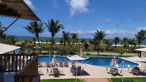 a swimming pool with chairs and umbrellas and the ocean at Village 2 suítes beira mar Itacimirim in Camaçari