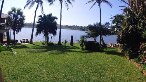 a lawn with palm trees and a body of water at The Lagoon Flat, 53 Nkwazi Drive in Zinkwazi Beach