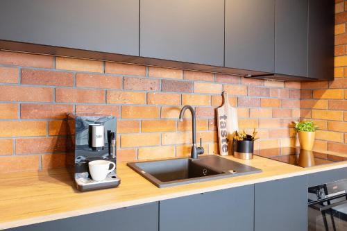 um balcão de cozinha com um lavatório e uma parede de tijolos em KOBIELA APARTMENTS Dębowe Tarasy em Katowice