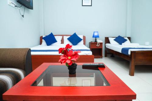 Cette chambre comprend deux lits et une table avec une fleur rouge. dans l'établissement SATK INN Jaffna, Kokkuvil, 