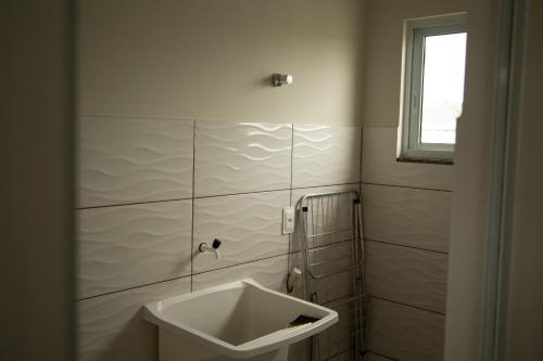 baño blanco con lavabo y ventana en Aloha Bratz Apartments 5, en Palhoça