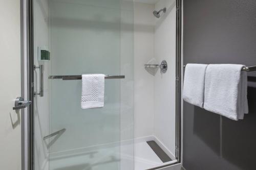 een badkamer met een douche, witte handdoeken en een glazen deur bij Courtyard by Marriott Norwalk in Norwalk