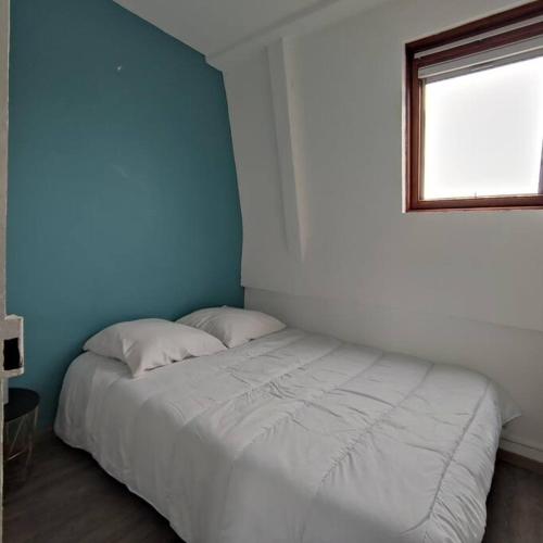 un letto bianco in una camera blu con finestra di L'Arche, appartement sur les toits d'Etretat a Étretat