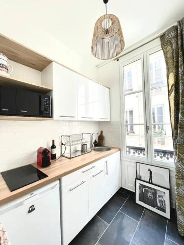 une cuisine avec des armoires blanches, un évier et une fenêtre dans l'établissement Brand new Flat in Paris, à Paris