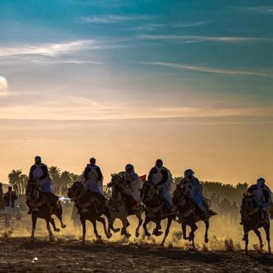 a group of people riding horses on a field at Faima in Douz